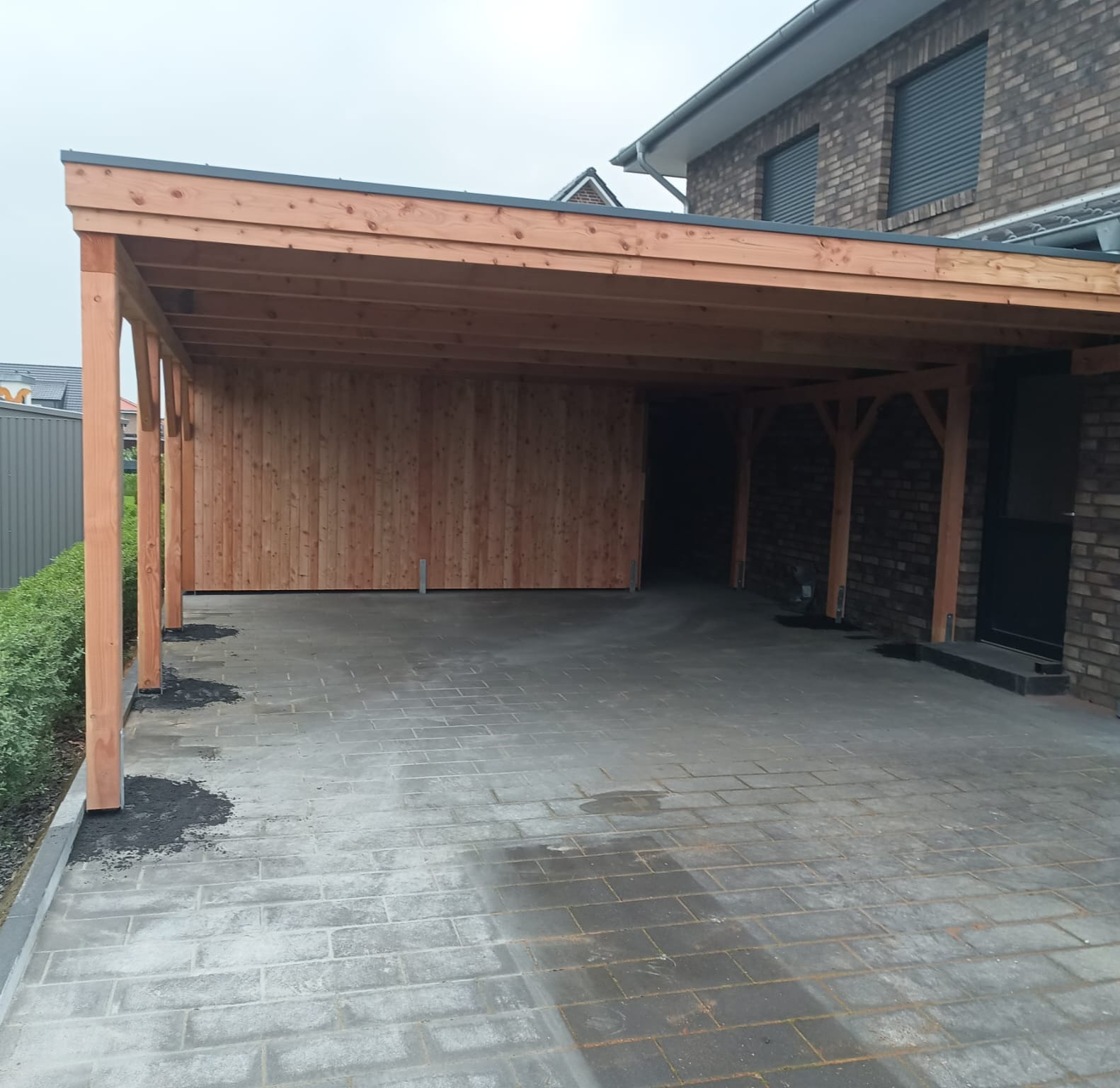 Großer Holz-Carport an einem Klinkerhaus mit Pflasterboden