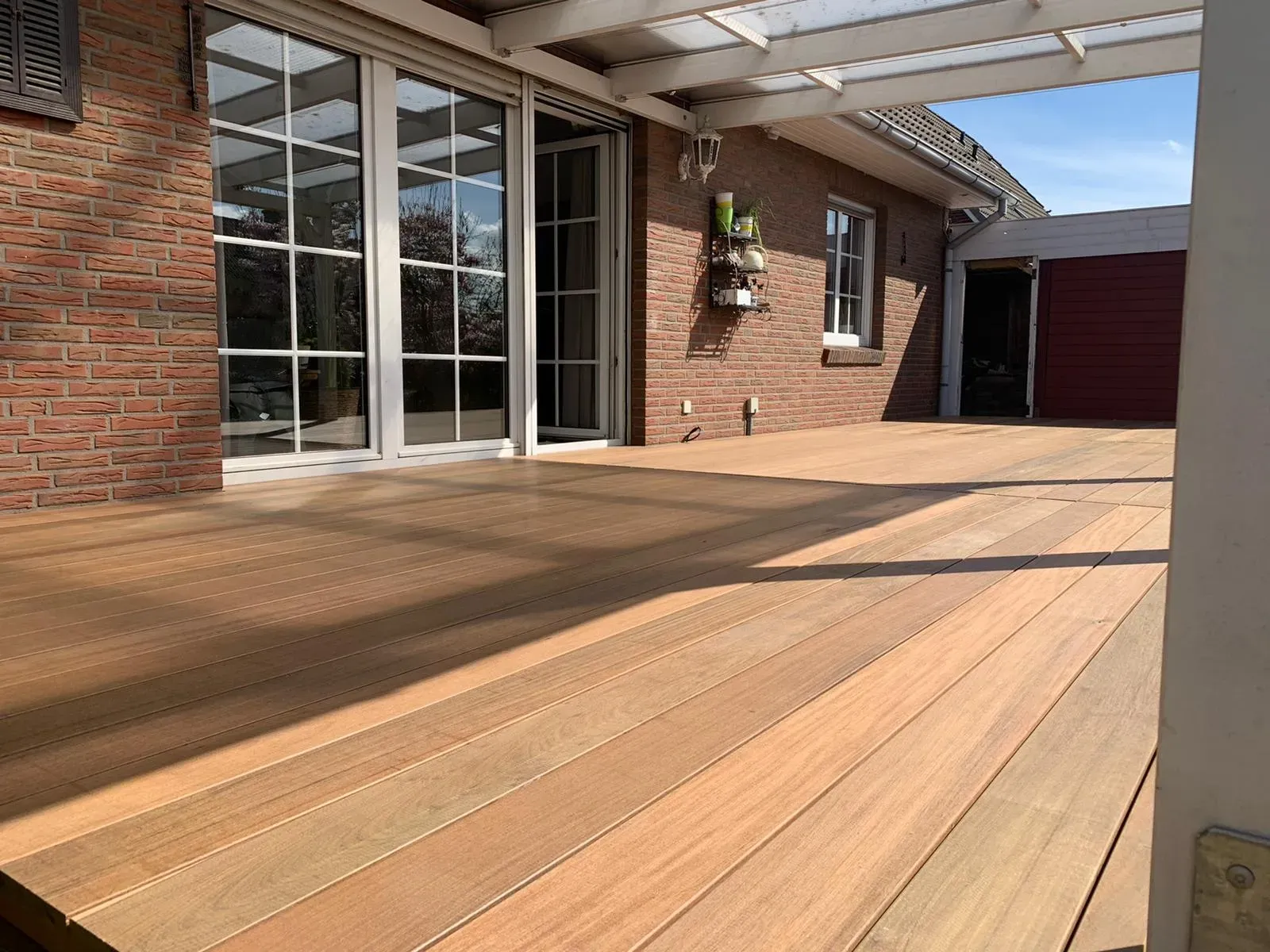 Fertig verlegte Holzterrasse aus warmem Hartholz vor der Terrassentür eines Backsteinhauses in Dollern